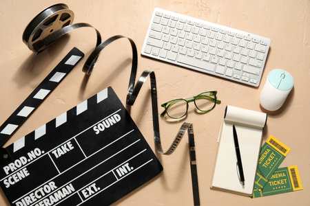 Movie clapper with reel, eyeglasses, computer keyboard, mouse and notebook on beige backgroundの写真素材