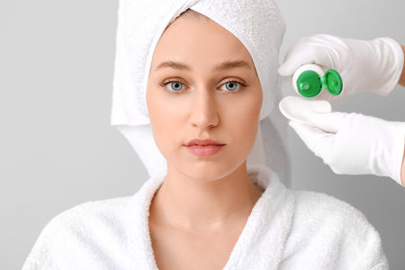 Beautician applying cosmetics on face of young woman against gray background