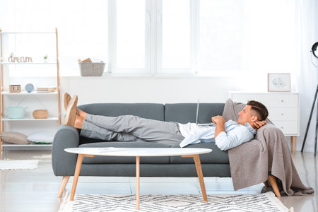 Young man with laptop relaxing on sofa at homeの写真素材