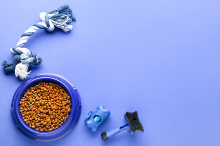 Bowl of dry pet food, toy, waste bags and grooming brush on color backgroundの写真素材