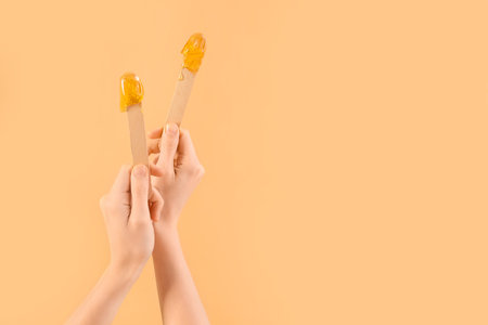 Female hands holding spatulas with sugaring paste on beige backgroundの写真素材