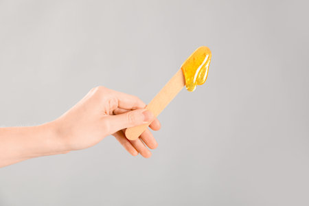 Female hand holding spatula with sugaring paste on light backgroundの写真素材