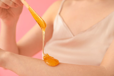 Young woman applying sugaring paste onto her arm against pink background, closeupの写真素材