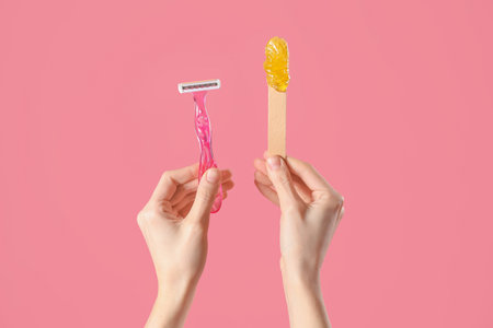 Hands holding spatula with sugaring paste and razor on pink background. hair removal conceptの写真素材