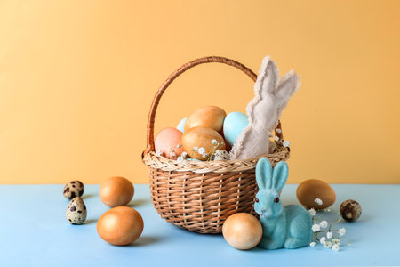 Basket with Easter eggs, bunnies and gypsophila flowers on blue table against beige backgroundの写真素材