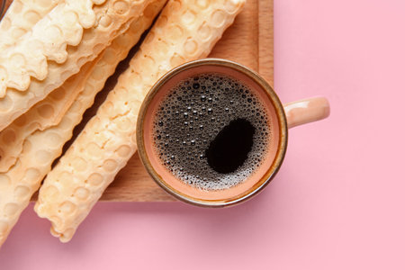 Board with delicious wafer rolls and cup of coffee on pink backgroundの写真素材