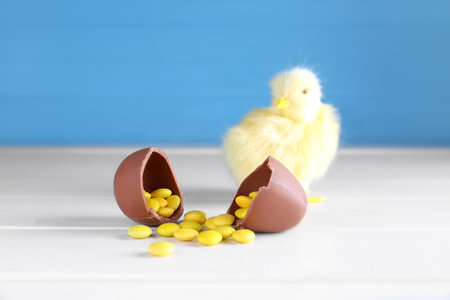 Baby chicken and chocolate Easter egg with candies on white wooden table against blue backgroundの写真素材