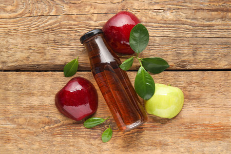 Glass bottle of fresh apple cider vinegar and fruits on wooden backgroundの写真素材