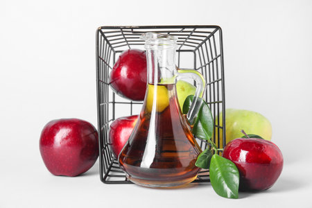 Glass bottle of fresh apple cider vinegar and overturned basket with fruits on white backgroundの写真素材