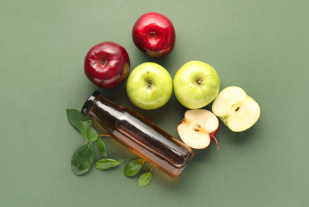 Glass bottle of fresh apple cider vinegar and fruits on green backgroundの写真素材