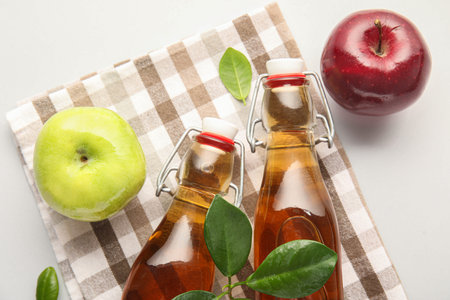 Glass bottles of fresh apple cider vinegar and fruits on gray background