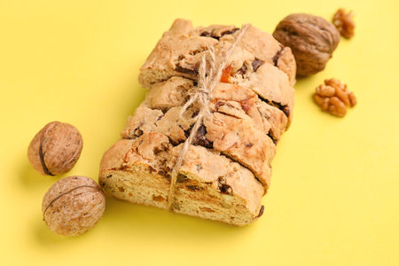 Delicious biscotti cookies tied with thread and walnuts on yellow background