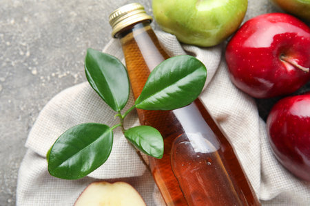 Glass bottle of fresh apple cider vinegar and fruits on gray grunge backgroundの写真素材