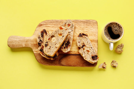 Board with delicious biscotti cookies and cup of coffee on yellow backgroundの写真素材