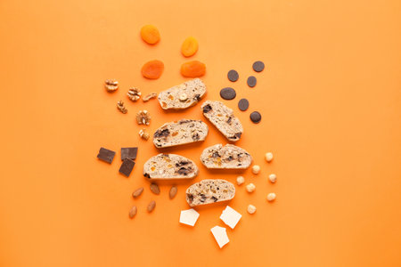 Composition with delicious biscotti cookies, nuts, chocolate and dried apricots on orange backgroundの写真素材