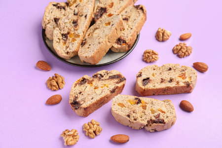 Plate with delicious biscotti cookies and nuts on lilac backgroundの写真素材