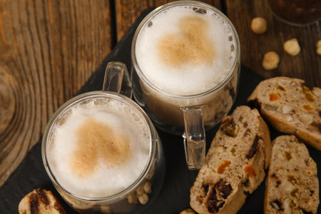 Slate board with delicious biscotti cookies and cups of coffee on wooden backgroundの写真素材