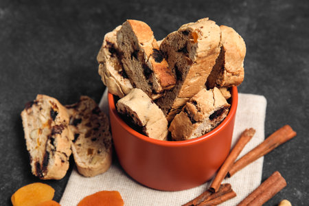 Bowl with delicious biscotti cookies, dried apricots and cinnamon on black grunge backgroundの写真素材