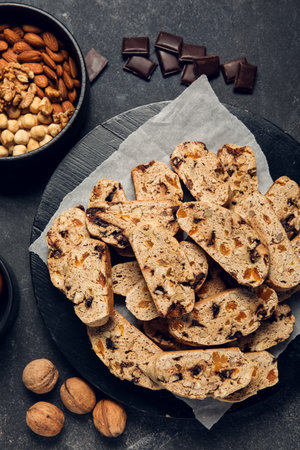 Board with delicious biscotti cookies, nuts and chocolate on black grunge backgroundの写真素材