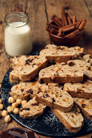 Board with delicious biscotti cookies, hazelnuts and glass of milk on wooden backgroundの写真素材
