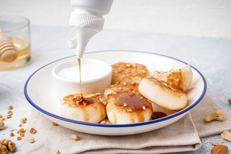 Pouring of caramel syrup onto tasty cottage cheese pancakes on table, closeupの写真素材