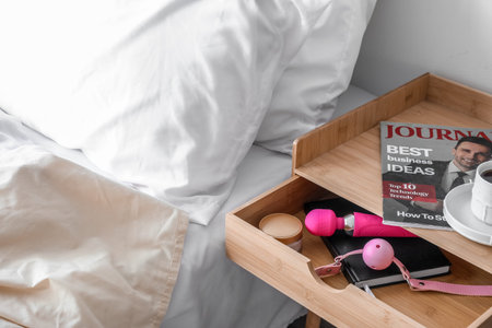 Open drawer with sex toys, notebook and cream in bedroom, closeup