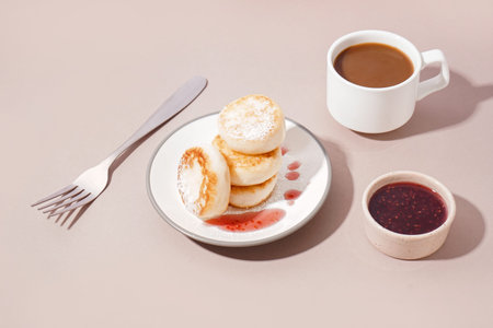Plate with delicious cottage cheese pancakes, strawberry jam and cup of coffee on color background