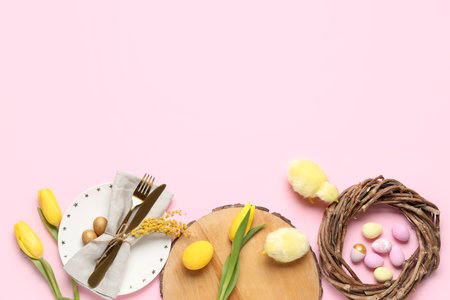 Table setting with Easter eggs, wreath and flowers on pink background