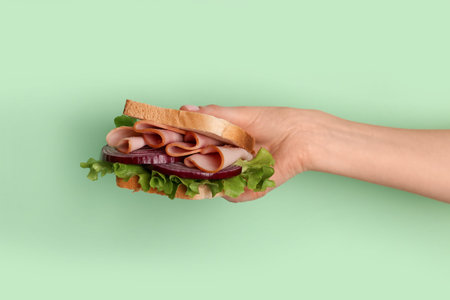 Female hand holding delicious ham sandwich on green background