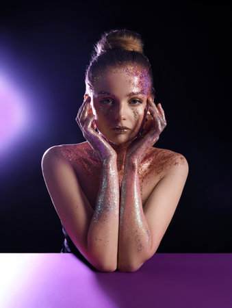 Beautiful young woman with glitter makeup at purple table on dark backgroundの写真素材