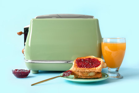 Modern toaster, glass of juice and toasts with jam on blue backgroundの写真素材