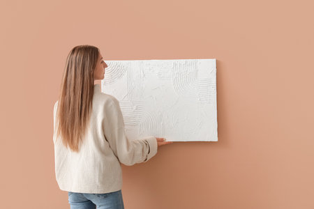 Young woman painting hanging on beige wallの写真素材