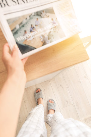 Young woman in soft slippers and newspaper at homeの写真素材