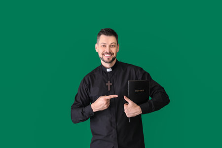 Handsome priest with Bible on color background