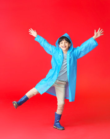 Cute little boy in raincoat on color backgroundの写真素材