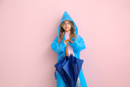 Cute little girl in raincoat and umbrella on color backgroundの写真素材