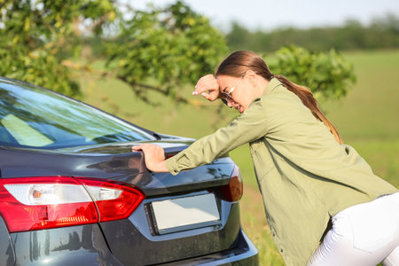 Young woman trying to push broken car on roadの写真素材