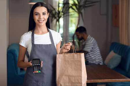Young waitress with food for delivery and payment terminal in restaurantの写真素材