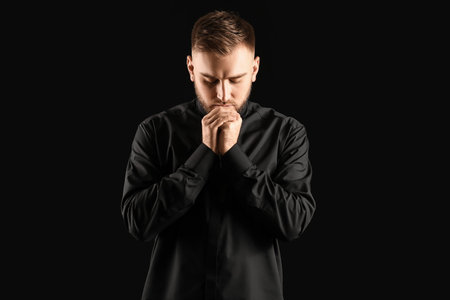 Young priest praying to God on dark backgroundの写真素材