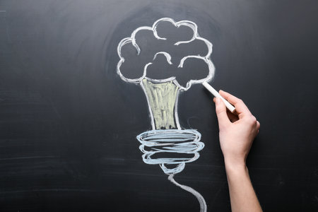 Female hand drawing lightbulb on chalkboardの写真素材