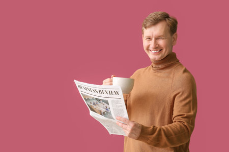 Handsome man with cup of tea and newspaper on color backgroundの写真素材