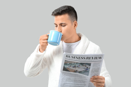 Handsome young man with cup of tea and newspaper on gray backgroundの写真素材