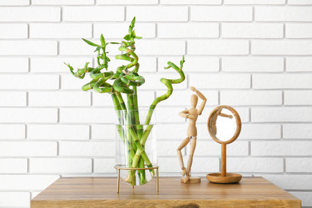 Vase with bamboo plant, wooden mannequin and mirror on table near brick wallの写真素材