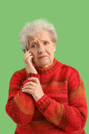 Sad senior woman talking by mobile phone on green backgroundの写真素材