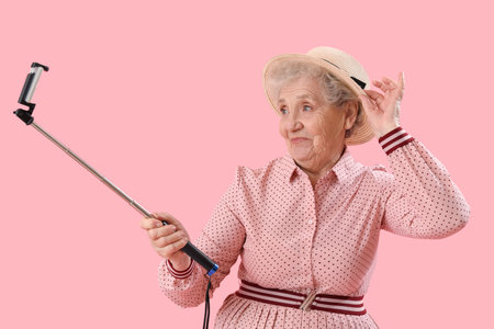 Senior woman with mobile phone taking selfie on pink backgroundの写真素材
