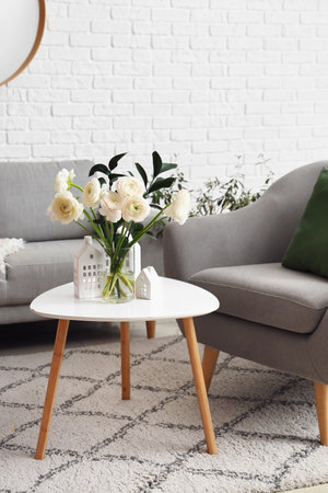 Vase with ranunculus flowers and house candle holders on table in living roomの写真素材
