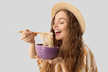 Young woman with bowl of Chinese noodles on light background, closeup