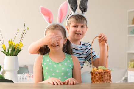 Little boy with basket of Easter eggs closing his sister's eyes in the kitchen