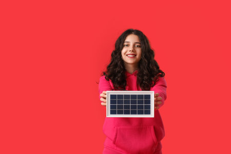 Teenage girl with portable solar panel on red backgroundの写真素材