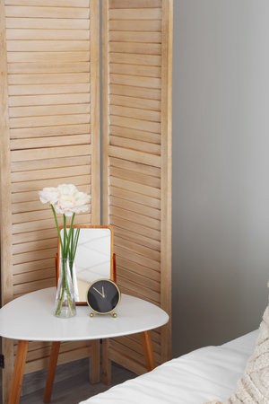 Vase with ranunculus flowers, alarm clock and mirror on table in bedroomの写真素材